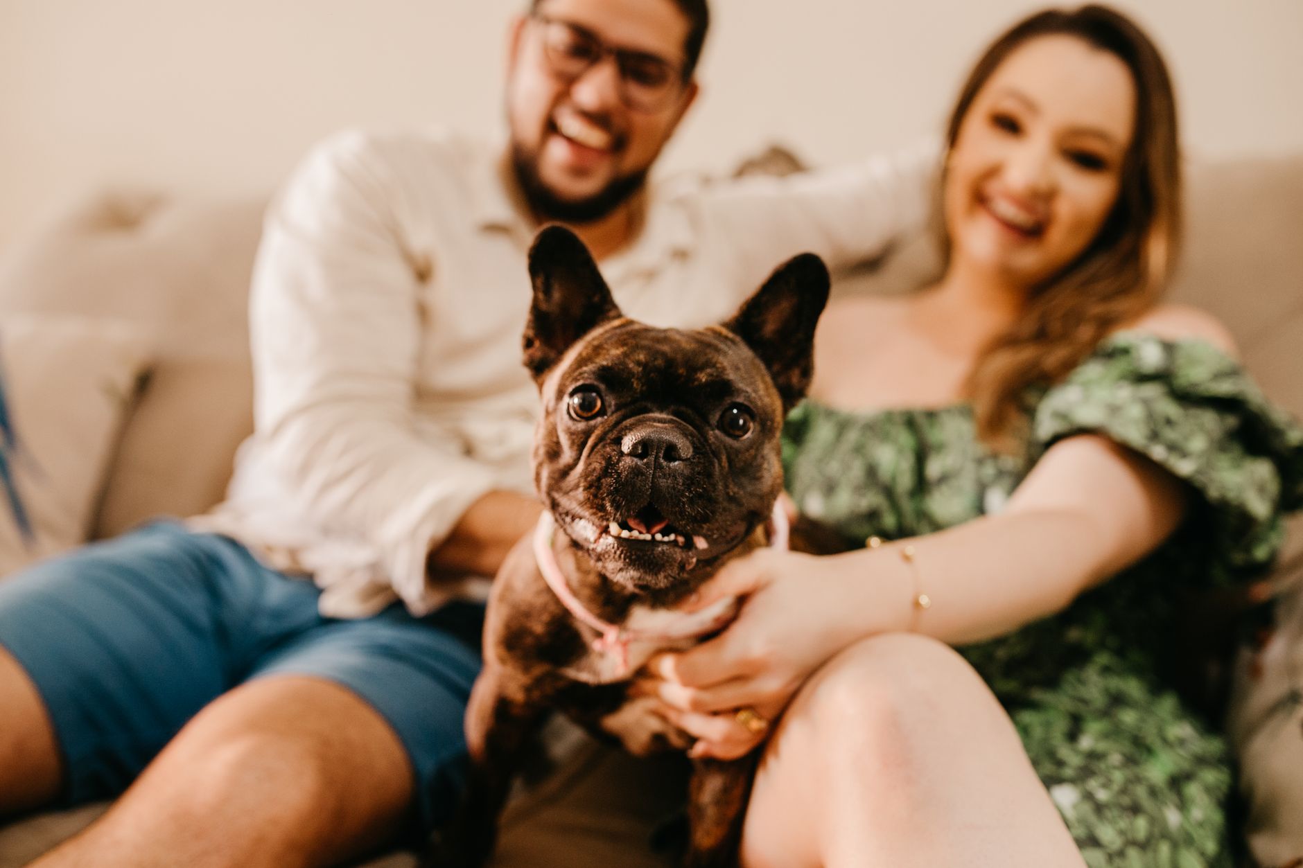 A joyful couple relaxing with their adorable French bulldog indoors.