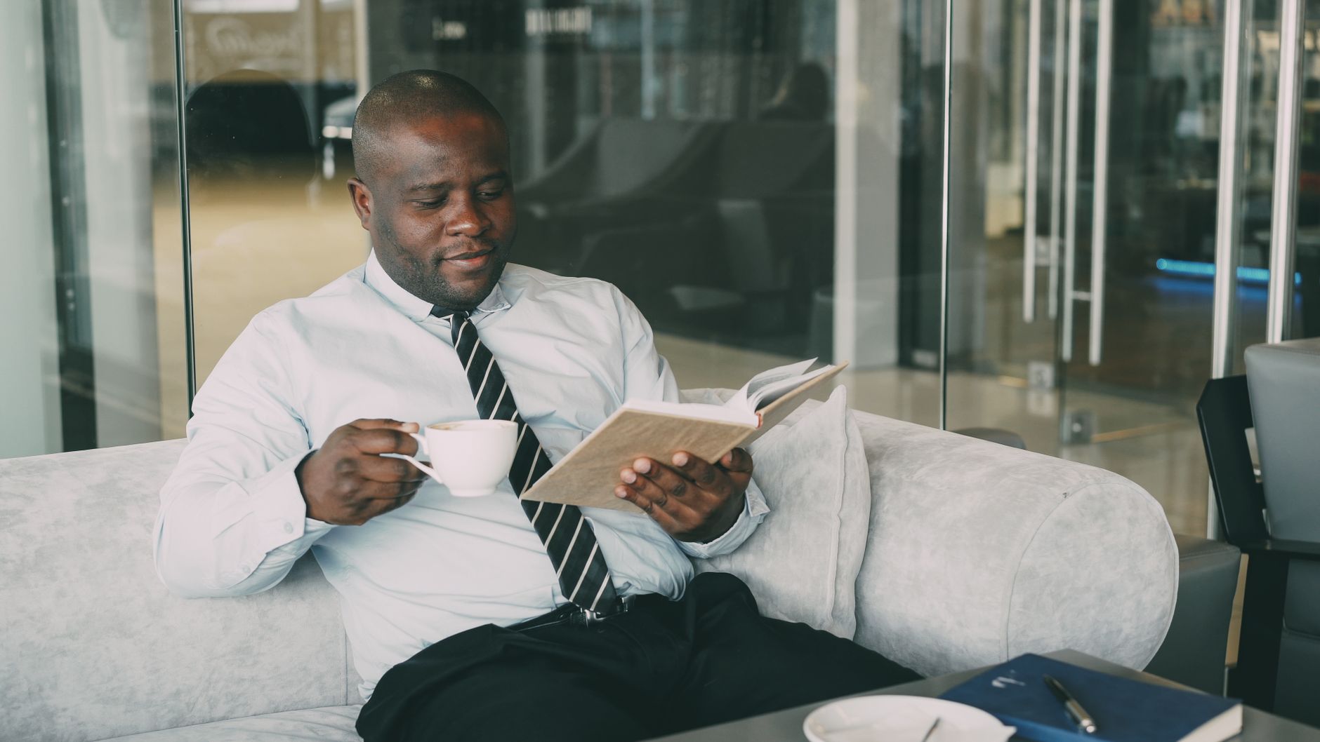 A businessman relaxes with a coffee and book in a modern indoor setting, embracing leisure.