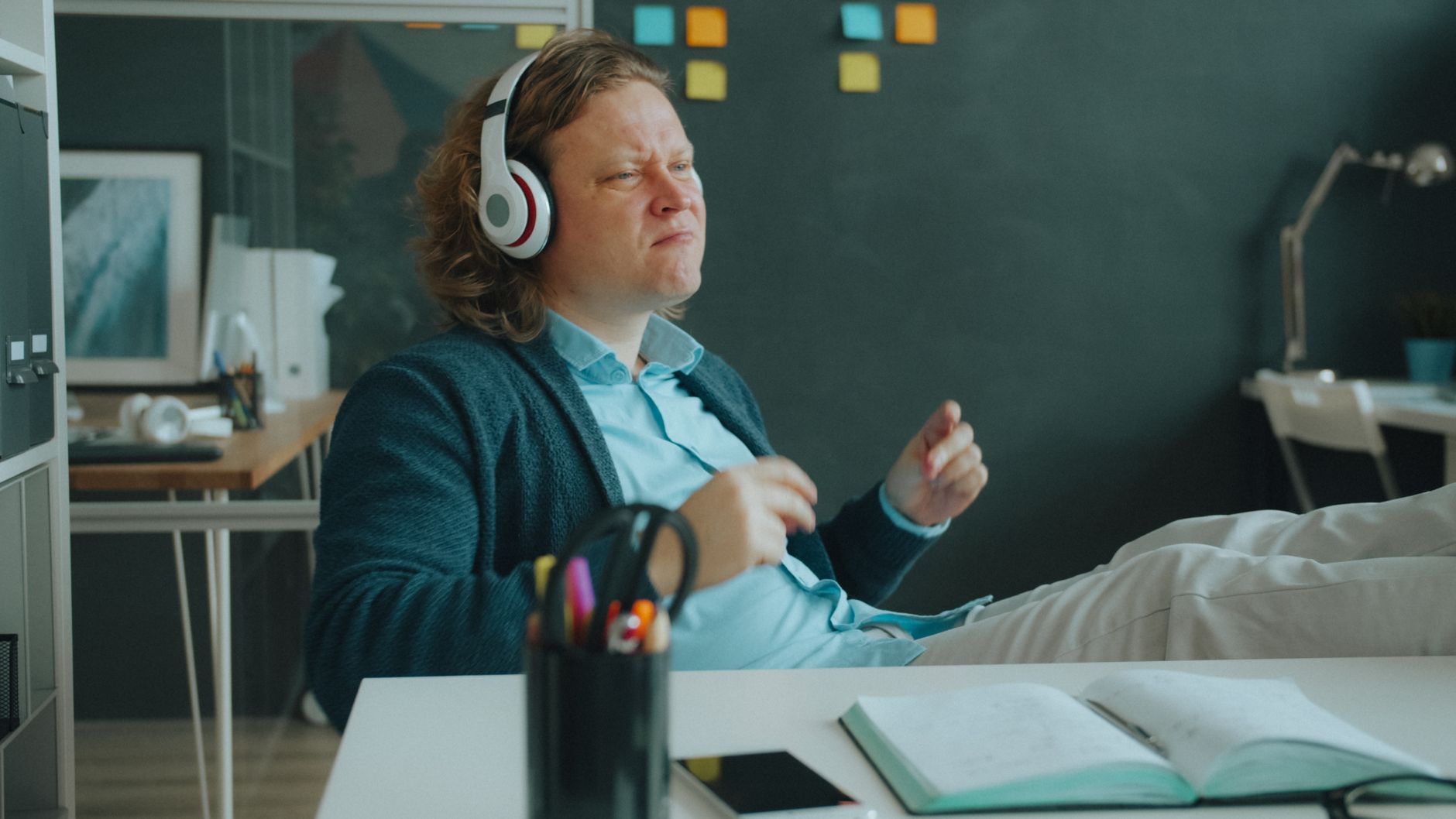 A relaxed man with headphones sits at a desk, enjoying music in a modern office setting.