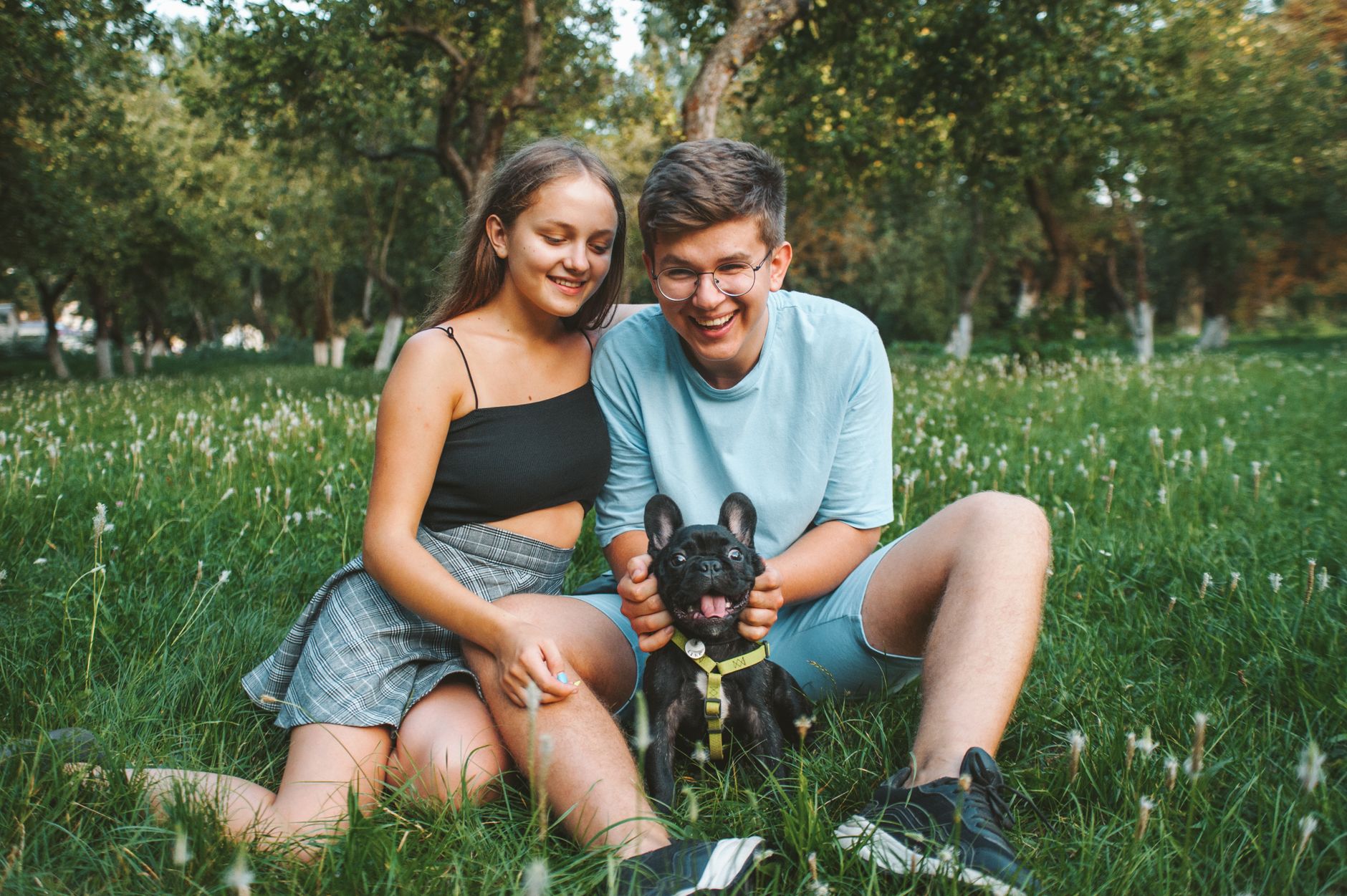 Young couple enjoying a day outdoors with their French Bulldog in a sunny park.